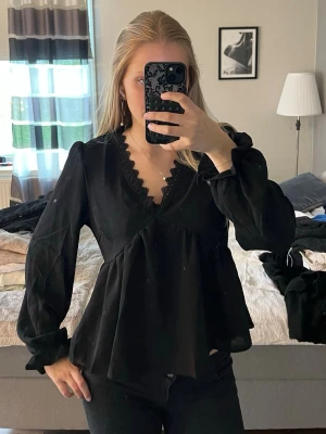Svart blus med spetsdetalj - Trendig svart blus med v-ringning och fina spetsdetaljer längs urringningen. 