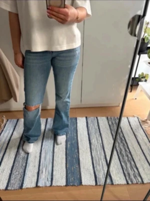 Ljusblå bootcut jeans med hål - Säljer ett par ljusblå bootcut jeans med hål på vänstra benet.. Bra i passform, elastisk material. Bekväma. Fickor i bak 