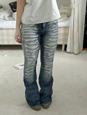 Jaded London bootcut jeans med slitningar - Säljer ett par blå bootcut jeans med kraftiga slitningar och blekta detaljer framtill. Jeansen har låg midja och klassisk femficksdesign. Perfekta för dig som gillar en edgy och trendig stil. Materialet är denim i bomull.