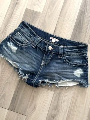 Mörkblå jeansshorts från Gina14+ - Snygga mörkblå jeansshorts med slitna detaljer och fransig kant. Klassisk femficksmodell med låg midja och dekorativa sömmar på bakfickorna. Perfekta för varma dagar och en avslappnad stil. Storlek xs men passar s