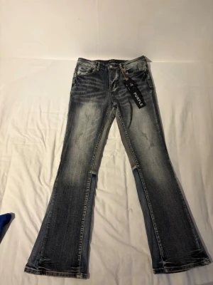 Bootcut jeans från Purple, blå tvätt - Snygga bootcut jeans från Purple i blå tvätt med slitningar och ljusa partier. Klassisk femficksmodell med dragkedja och knapp. Jeansen har en trendig utsvängd passform och är tillverkade i denim. Perfekta för en cool och avslappnad stil.