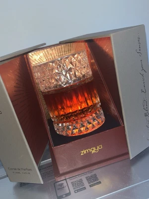 Sharaf Blend de Parfum från Zimaya - Lyxig parfym från Zimaya i elegant kristalliknande glasflaska med mönstrad yta. Flaskan har en varm bärnstensfärgad vätska och levereras i en exklusiv, guldskimrande förpackning med gulddetaljer. Doften är Extrait de Parfum och flaskan rymmer 100 ml. Helt ny knappt använt 