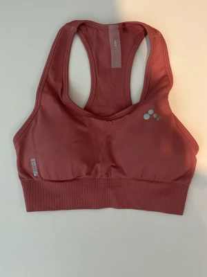 Rosa sport-bh från Only Play - Sport-bh i dämpad rosa färg från Only Play. Modellen har brottarrygg och bred resår nedtill för extra stöd. Materialet är stretchigt och mjukt, perfekt för träning eller yoga. Diskret logga framtill och sömlös design för en clean look.