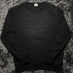 C.P. Company Sweatshirt  - Klassisk svart C.P. Company-sweatshirt med broderad logga framtill. Storlek L, men passar även M beroende på önskad passform. Stilren, lättmatchad och perfekt till vardags/streetwear.  QR-kod finns som äkthetsbevis. Skick enligt bilder.