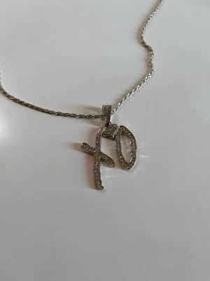 XO chain - the Weeknd  - Snyggt halsband i silverfärg med ett XO-hänge dekorerat med små glittrande stenar. Kedjan har en tvinnad design och hänget har en modern, handskriven stil. Perfekt accessoar för dig som gillar statement-smycken och vill sticka ut.