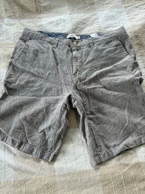 Grå linneshorts med fickor - Snygga grå shorts i linne med klassisk passform och sidofickor. De har bälteshällor, knappgylf och en bakficka med knapp. Perfekta för varma dagar och ger en avslappnad men stilren look.