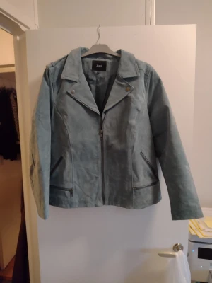 Ljusblå skinnjacka från Zizzi - Snygg ljusblå skinnjacka från Zizzi med klassisk bikerkrage, dragkedja framtill och två snedställda fickor med dragkedja. Jackan har silverfärgade detaljer och en mjuk, matt finish som ger en cool look kostade som ny 1299:-