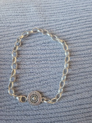Thomas Sabo silverfärgat armband - Stilrent armband från Thomas Sabo i silverfärgad metall med ovala länkar och en rund berlock med text och glittrande detalj i mitten. Perfekt accessoar för att lyfta din outfit med en cool touch.