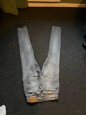 Ljusgrå slim fit jeans från tiger of sweden  - Säljer ett par ljusgrå slim fit jeans från Weekday med klassisk femficksmodell och snygga slitningar. Jeansen har normal midja, bälteshällor och knappgylf. Perfekta för dig som gillar en avslappnad men trendig stil.