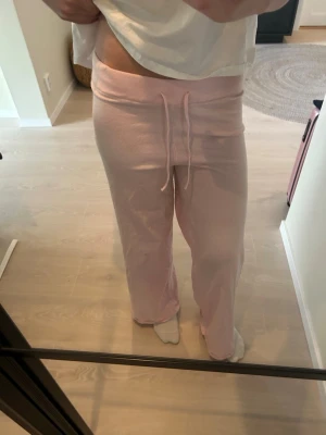 Ljusrosa mjuka loungewear-byxor - Supermysiga ljusrosa loungewear-byxor med bred resår och dragsko i midjan. Byxorna har raka ben och är tillverkade i ett mjukt, stretchigt material som passar perfekt för chill hemma. Perfekta för dig som vill ha något bekvämt och stilrent på dig.