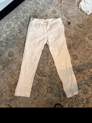 Vita linnebyxor med spänne - Snygga vita linnebyxor med raka ben och justerbart spänne i midjan. Perfekta för en avslappnad och stilren look. Byxorna har klassisk passform och är tillverkade i svalt linnematerial.