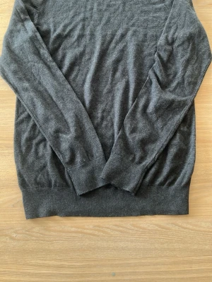 Mörkgrå bomullströja från dressman - Mjuk och stilren mörkgrå tröja i 100% bomull. Klassisk modell med rund hals och långa ärmar, perfekt för en clean och enkel look. Passar till det mesta och är superbekväm att bära.