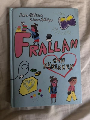 Frallan och kärleken - En charmig och färgglad barnbok med hårt omslag, skriven av Sara Ohlsson och illustrerad av Lisen Adbåge. Omslaget är ljusblått med tecknade figurer, hjärtan och pysselmotiv. Boken handlar om Frallan, skola, vänskap och kärlek.