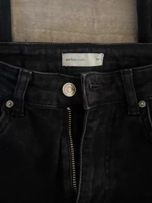 Svarta jeans från Gina - Säljer ett par svarta/urtvättade jeans från Perfect Jeans med klassisk femficksdesign och dragkedjegylf. Jeansen har bootcut ben och är tillverkade i ett denimtyg som känns slitstarkt. Perfekta för dig som gillar en enkel och stilren look.