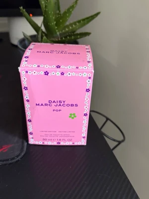 Daisy Pop parfym från Marc Jacobs - Daisy Pop från Marc Jacobs är en limited edition parfym i en söt rosa flaska med vita blommor och grön detalj på korken. Förpackningen är också rosa med blommönster. Flaskan rymmer 50 ml och har en lekfull och färgglad design.