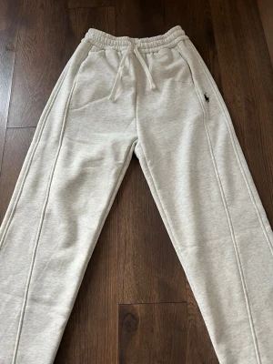 Grå mjukisbyxor från Ralph Lauren - Snygga ljusgrå mjukisbyxor från Ralph Lauren med dragsko i midjan och broderad logga på höften. Byxorna har raka ben, sidofickor och en bakficka. Perfekta för en chill och avslappnad stil. Storlek L men sitter som M