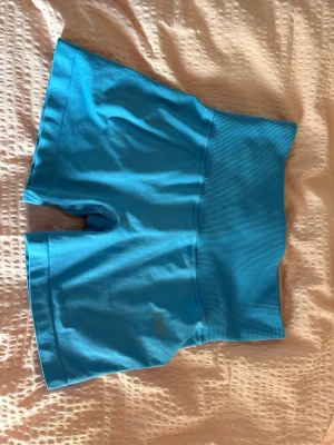Blåa ICANIWILL träningsshorts - Säljer ett par blå högmidjade träningstights-shorts från ICANIWILL. De har bred ribbad midja för extra stöd och en liten diskret logga på benet. Perfekta för gymmet eller löpning under sommaren.