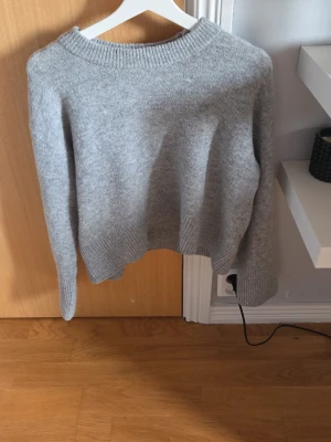 Grå stickad tröja med rund hals - Mysig grå stickad tröja med rund halsringning och ribbade muddar vid ärmslut och nederkant. Tröjan har en avslappnad passform och är perfekt för lager-på-lager-stil. Passar dig som gillar enkel och stilren design.