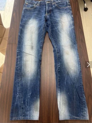 Tornado Mart Jeans - Säljer ett par blå jeans med raka ben och tydliga slitningar samt ljusa partier framtill. Jeansen har klassisk femficksmodell och är gjorda i denim. Perfekta för en avslappnad och trendig look. De är köpte från Japan. 