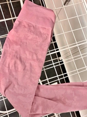 Rosa seamless leggings från Gymshark - Säljer ett par rosa seamless leggings från Gymshark med hög midja och diskret camo-mönster. De är stretchiga och har ribbad linning för extra komfort. Perfekta för träning eller chill dagar.