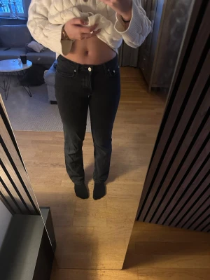 Svarta raka jeans med hög midja - Säljer ett par svarta jeans med rak passform och hög midja. Jeansen har klassisk femficksdesign, bälteshällor och knappgylf. Perfekta för dig som gillar en stilren och enkel look.