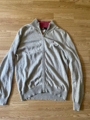 Morris zip - Tröja med hel dragkedja framtill. Kragen är ribbad och har en kontrasterande färg på insidan. Ärmsluten och nederkanten är också ribbade. En liten broderad logotyp finns på bröstet. Baksidan av armbågarna har runda applikationer i en kontrasterande färg. Mått kan fixas vid fråga!