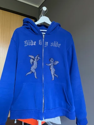 Blå rhinestone hoodie - Blå rhinestone hoodie gjord av ett gammalt startup som hette side by side. Storlek M men den passar lite oversize. Det är nån enstaka rhinestone som låssnat men inget som märks. Utöver det, inga defekter. 