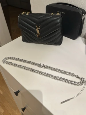 Silverfärgat kedjebälte från Michael Kors - Säljer ett stilrent kedjebälte i silver från Michael Kors. Bältet har en grov kedja och MK-logga framtill, perfekt för att lyfta en outfit. Justerbar längd med kedja i slutet för flexibel passform.