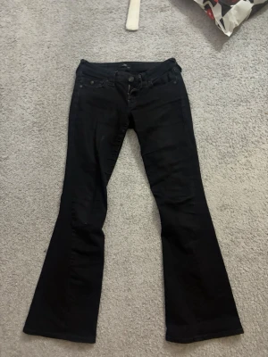True religion Svarta bootcut jeans  - I storlek 26 använda men bra skicka syns så bilderna att dom är tvättade. Säljer ett par svarta bootcut jeans  med klassisk femficksdesign och normalhög midja. Jeansen har utsvängda ben och är tillverkade i ett stretchigt bomullsmaterial för skön passform. Perfekta för dig som gillar en retroinspirerad look.