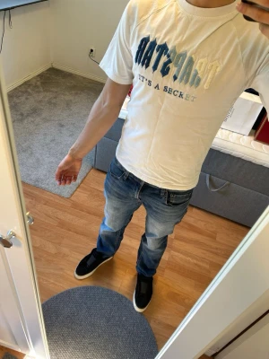 Vit Trapstar T-shirt - Säljer en vit t-shirt med trycket. TRAPSTAR och 'IT’S A SECRET' och stora bokstäver i olika blå nyanser på bröstet. T-shirten har normal passform och korta ärmar. Perfekt för dig som gillar enkel men snygg stil. Passar fint för sommaren
