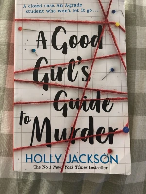 A Good Girl's Guide to Murder - Spännande thrillerbok på engelska av Holly Jackson. Omslaget är vitt med rutmönster, röda trådar och nålar som ger en true crime-känsla. Perfekt för dig som gillar mysterier och deckare. Pocketutgåva från Electric Monkey.