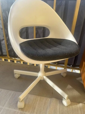 Vit snurrstol med svart sits - Modern snurrstol i vit plast med rundad rygg och öppning i ryggen. Sitsen är stoppad och klädd i svart tyg. Stolen har fem hjul och passar perfekt till skrivbordet eller plugghörnan.