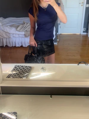 Mörkblå tight topp med kort ärm - Säljer en mörkblå topp med tight passform och korta ärmar. Toppen har en enkel, stilren design utan synliga detaljer och är perfekt att matcha med kjol eller jeans. Materialet känns mjukt och stretchigt, troligen bomull eller polyester.