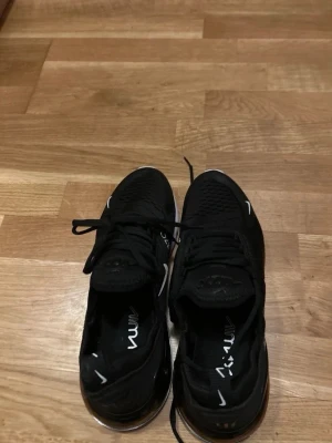 Nike Air Max 270  - storlek 43. Svarta Nike Air Max 270 sneakers med vit sula och tydlig Air-enhet i hälen. Ovandelen är i mesh för bra ventilation och har vita detaljer samt logga på sidan och tungan. Skorna har klassisk snörning och en sportig, modern look.