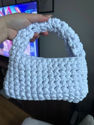 Handvirkad vit handväska - Säljer en handvirkad vit handväska med chunky struktur och kort handtag. Väskan har en rektangulär form och är gjord av tjockt garn, vilket ger en trendig och unik look. Perfekt accessoar för dig som gillar stickat och handgjorda detaljer.