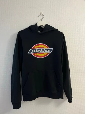 Svart Dickies hoodie med logga - Säljer en svart hoodie från Dickies med stor färgglad logga på bröstet. Hoodien har huva och en klassisk känguruficka framtill. Tillverkad i mjukt material som passar perfekt för en avslappnad streetwear-look.