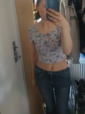 Blommig croppad topp med kort ärm - Söt croppad topp med blommigt mönster i ljusa färger. Toppen har korta ärmar, rundad halsringning och öppen rygg. Perfekt för varma dagar och enkel att matcha med jeans eller kjol.