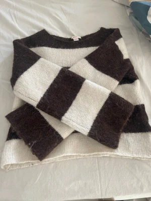 Randig stickad tröja i mohairmix - Säljer en fluffig stickad tröja med breda bruna och vita ränder. Tröjan har en avslappnad passform, rund halsringning och långa ärmar. Materialet ser ut att vara en mjuk mohair- eller ullmix som ger en mysig känsla.