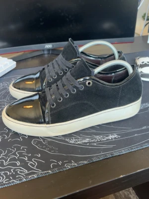 Lanvin skor - Snygga svarta sneakers med ovandel i mocka och glansiga lackdetaljer på tån. Skorna har svarta skosnören, metallfärgade öljetter och vit sula. Perfekta för dig som vill ha en stilren men ändå unik look.