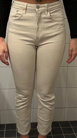 Beiga raka jeans med hög midja - Snygga beiga jeans med rak passform och hög midja. Jeansen har klassiska bakfickor och stängs med dragkedja och knapp. Materialet är mjukt och stretchigt för extra komfort. Perfekta för en clean och stilren look.