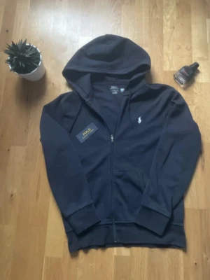 Polo Ralph Lauren - Svart hoodie från Polo Ralph Lauren med broderad logga på bröstet och klassisk huva med dragsko. Tillverkad i mjukt material som känns skönt mot huden. Perfekt för dig som gillar stilrena och tidlösa plagg. Pris kan diskuteras helt ny bara testad men formen passade inte mig så säljer vidare