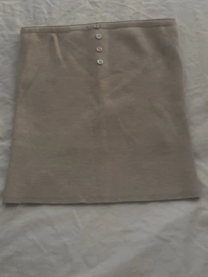 Beige stickad topp från Gina Tricot - Beige stickad topp från Gina Tricot med rak passform och fyra dekorativa knappar framtill. Tröjan är enkel och stilren, perfekt till sommaren och passar till många olika outfits.