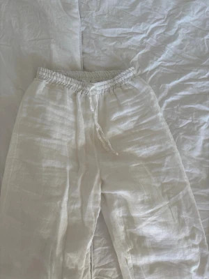 Vita linnebyxor  - Säljer ett par vita linnebyxor från Design by Si i storlek S. Byxorna har avslappnad passform, resår i midjan. Tillverkade i svalt och luftigt linne, perfekta för varma dagar.