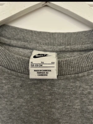Grå sweatshirt från Nike  - Klassisk grå sweatshirt från Nike med broderad vit logga på bröstet. Tröjan har rund halsringning och ribbade muddar vid halsen. Perfekt för en avslappnad och sportig stil.