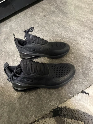 Svarta Nike Air Max 270 sneakers - Helt nya Snygga helsvarta Nike Air Max 270 sneakers med luftig mesh och syntetmaterial. Ikonisk Air Max-sula för extra komfort och cool look. Lågt skaft och diskret Nike-logga på sidan. Perfekta för dig som gillar streetwear och sportig stil. Kartongen finns tyvärr inte med
