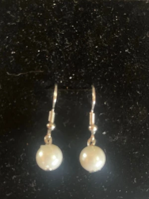 Silvriga örhängen med vita pärlor - Snygga örhängen med vita, runda pärlor som hänger i silvriga krokar. Klassisk och stilren design som passar till många olika looks. Perfekta för dig som gillar en enkel men elegant accessoar.