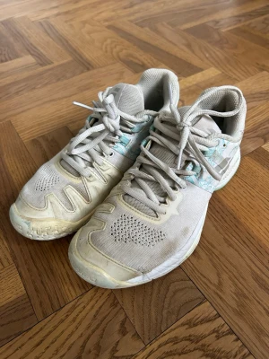 Padelskor Babolat *37* - Säljer ett par beige sneakers med turkosa mönsterdetaljer vid snörningen. Skorna har meshpaneler för extra ventilation och en robust sula. Perfekta för dig som gillar sportig stil och vill ha något bekvämt till vardags. Klassisk snörning och låg modell.
