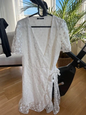 Vit spetsklänning omlott från Gina - Säljer en vit kort spetsklänning från gina med omlottmodell och knyt i midjan. Klänningen har korta ärmar, v-ringning och fina spetsdetaljer över hela plagget. Perfekt för sommarens alla tillfällen!