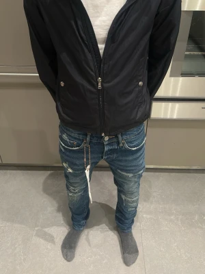 Purple jeans - Säljer ett par blå jeans med slitningar och tvättade detaljer. Modellen är slim fit med låg midja och har en silverfärgad kedja i hällan. Jeansen har klassiska fem fickor och vita sömmar som kontrast. Perfekta för en trendig streetwear-look. Storlek 28 men sitter som 27