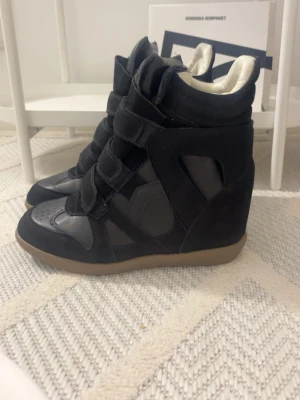 Svarta wedge sneakers  - Säljer ett par svarta wedge sneakers med högt skaft och kardborreband. Skorna har en cool mix av mocka och läderdetaljer samt beige sula. Insidan är vit och de har en chunky siluett som sticker ut.